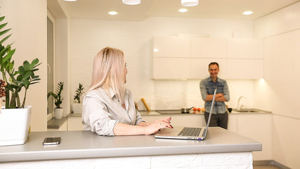 Business couple in kitchen, man preparing breakfast, woman using laptop