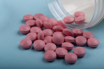 pink pills pouring out of the medicine bottle on blue background; medical treatment and safe use drug concept. closed up and selective focus 