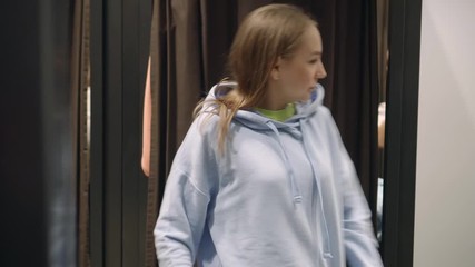 Pretty woman tries on a blue sweatshirt spinning in front of a mirror, shopping