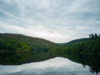pequeñas colinas verdes con cielo nublado reflejadas en agua calmada
