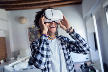 Happy afro-american young man using his virtual reality glasses while standing at home.