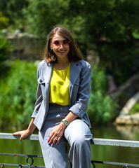 The woman in a gray stylish suit among greens sits in the park and has a rest. Portrait and emotions.