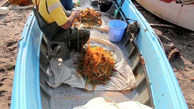 Fisher in rubber trousers and boot siting in his boat and pile up fishing net for angling at open sea. Photo - JPEG video codec