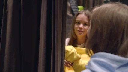 Girlfriends shopping together. Young beautiful woman trying on yellow sweatshirt