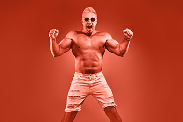 Excited Muscular strong expressive man with naked torso in fashion neon coral light. Sexy pumped-up...