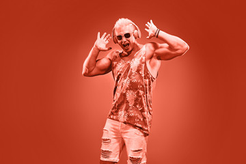Fashion Excited DJ man dance with expression in neon coral light. Sexy emotional Handsome pumped-up blonde guy listen to music. Art neon fashionable style. Music festival nightclub, party concept