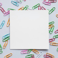 Elevated view of square shaped cardboard paper and many paper clips on grey background