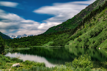 Obraz premium Landscape, mountain lake with clear water in the foreground, against the top of the mountains with a glacier and a blue sky with clouds.