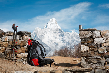 A backpack, hiking poles and a mug on the background of Mount Ama Dablam. The mountain is blurred....
