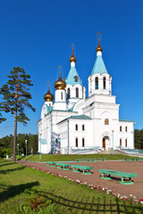 Holy Trinity Cathedral on a sunny summer day on background of blue sky. Church cozy courtyard with green lawns and benches. Angarsk, Irkutsk region. Beautiful cityscape