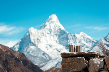 Two cups are on the stones in focus. Mount Ama Dablam is blurred. Everest trekking base camp Nepal.