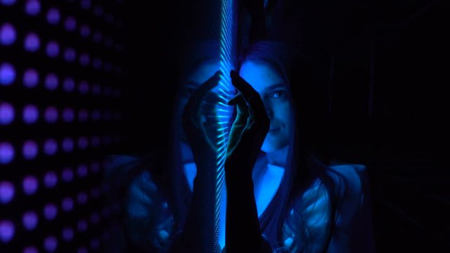 Millennial pretty girl near glowing bright colored LED SMD video wall with high saturated patterns