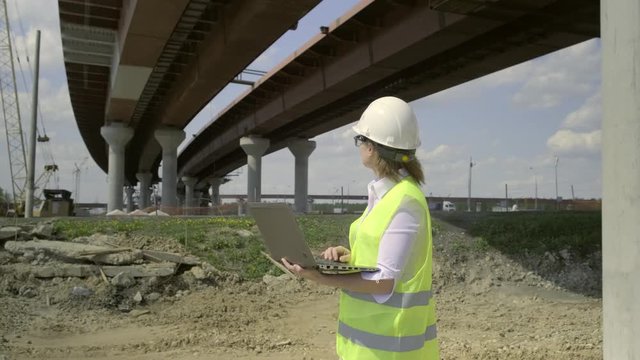 Engineer woman with laptop under overpass under construction. manager of repair works working on a computer while standing at construction site.
