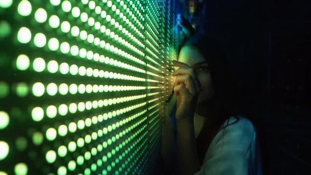 Millennial pretty girl near glowing bright colored LED SMD video wall with high saturated patterns