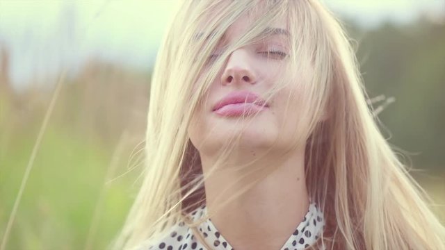 Portrait of beauty girl with fluttering white hair enjoying nature outdoors. Flying blonde hair on the wind. Beautiful young woman face closeup. Slow motion 4K UHD video footage. 3840X2160