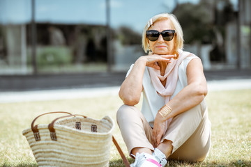 Lifestyle portrait of an elegant senior business woman dressed in white shirt sitting outdoors in the city. Concept of an active people during retirement age
