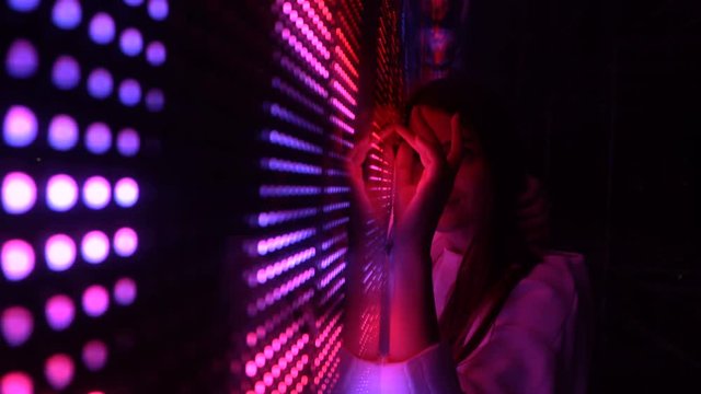 Millennial pretty girl near glowing bright colored LED SMD video wall with high saturated patterns