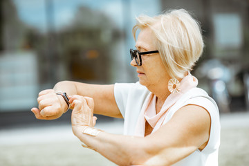 Senior woman using smart watch outdoors. Concept of using modern technologies by elderly people