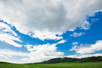 Blue sky with white clouds, fields and meadows with green grass, on the background of mountains. Composition of nature. Rural summer landscape.