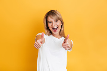 Happy young pretty blonde woman posing isolated over yellow wall background dressed in white casual t-shirt.