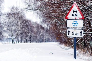 Snow covered road, winter driving with sign - slippery