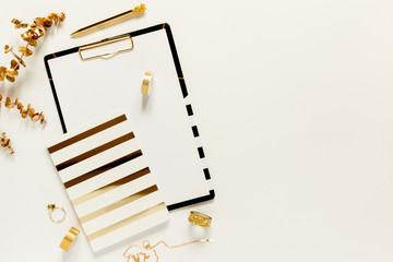 Flat lay desk table. Workspace with modern gold and black clipboard, notebook, stationery and decorations on white table. Copy space, top view