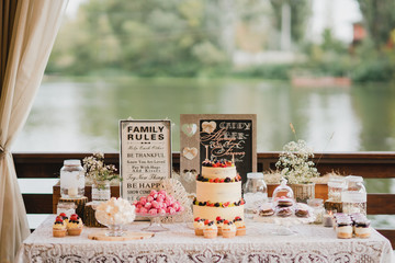 Candy bar with tasty desserts and appetizers at wedding reception. Decorated with flower compositions and candles. Sweet food, dessert, buffet, catering table, restaurant.