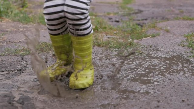 A small child shod in rubber boots, jumping in a dirty puddle after the rain.