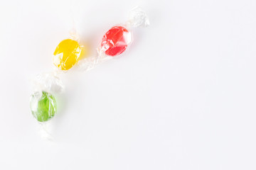 Multicolored fruit oval lollipops - red, yellow, green - on a light paper background. Sweet drops, taste of lemon, cherry, apple. Flat lay, minimalism, top view. Place for text.