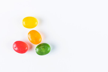 Multi-colored fruit oval lollipops - red, yellow, green, orange - on a light paper background. Sweet drops, taste of lemon, cherry, apple, orange. Flat lay, minimalism, top view. Copy space.