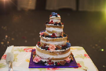 Stylish modern wedding cake. Beautiful dessert decorated with fresh flowers, fruits and greenery.
