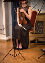 A young woman in black dress sitting on the chair holding violin