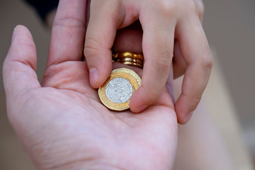 Kid hand giving two pound coin to his mam for donate to poor children,Crop view of children hand...