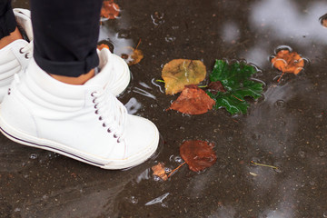 legs in white shoes jumping in the autumn puddles