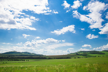 Blue sky with white clouds, fields and meadows with green grass, on the background of mountains. Composition of nature. Rural summer landscape.