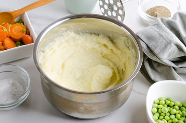 Delicious fresh cooked mashed potatoes in the pot, vegetables and spices on the white table