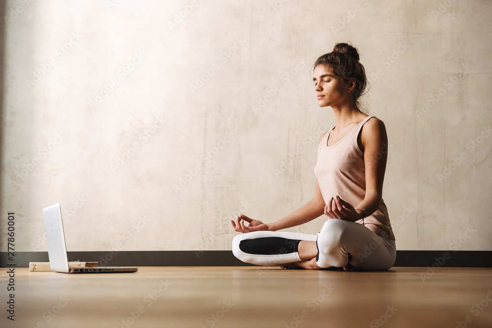 Wall mural photo of concentrated attractive woman meditating with zen fingers and using laptop while sitting on