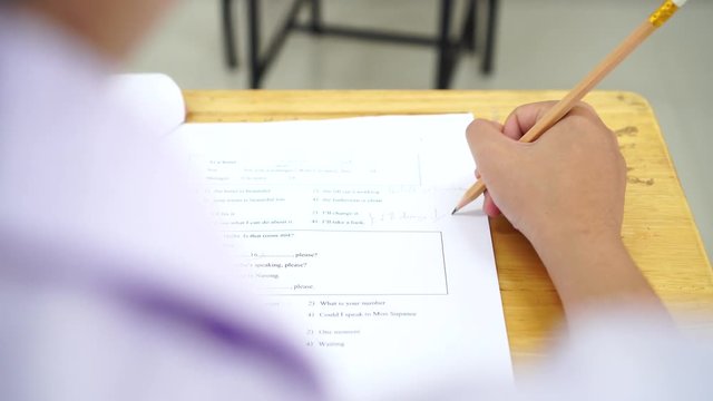 School Students hands taking exams, writing examination holding pencil on optical form of standardized test with answers sheet doing final exam in classroom. Education assessment Concept. Soft focus