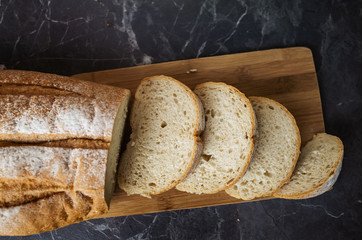 Fresh homemade white bread sliced on a wooden board on a dark gray table top. Concept of healthy natural food, home baking bread. Rustic, flat lay, top view, low key.