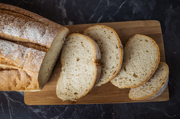 Fresh homemade white bread sliced on a wooden board on a dark gray table top. Concept of healthy natural food, home baking bread. Rustic, flat lay, top view, low key.
