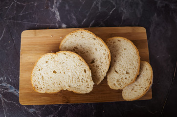 Fresh homemade white bread sliced on a wooden board on a dark gray table top. Concept of healthy natural food, home baking bread. Rustic, flat lay, top view, low key.