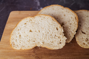 Fresh homemade white bread sliced on a wooden board on a dark gray table top. Concept of healthy natural food, home baking bread. Rustic, flat lay, top view, low key.