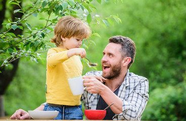 Fototapeta premium Feeding baby. Menu for children. Family enjoy homemade meal. Father son eat food and have fun. Food habits. Little boy with dad eating food nature background. Summer breakfast. Healthy food concept