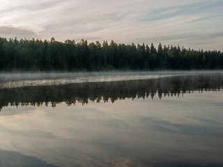 Foggy and mystical lake landscape before sunrise. All silhouettes are blurry and unclear. Vaidavas lake, Latvia
