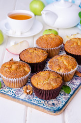 Homemade crispy apple muffins with walnuts and cinnamon on a white wooden background.