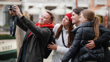 The company of four friends are photographed and take a selfie at the Venice waterfront.