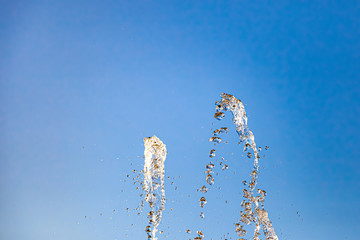 City fountain with splashes and tops jets of water frozen in the air on a clear summer day against the blue clear sky. Freshness and benefits of fluid.