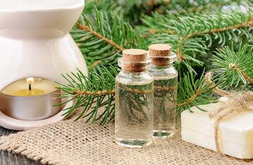 Two bottles of spruce essential oil, natural soap and fir branches behind on linen napkin.