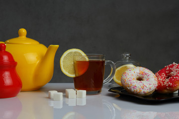 Cup of tea, donuts and yellow kettle on grey background