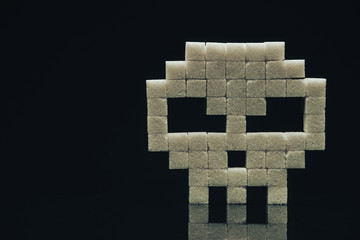 Skull with sugar cubes on a  black glass table background. Concept sweet kill or unhealthy diet .